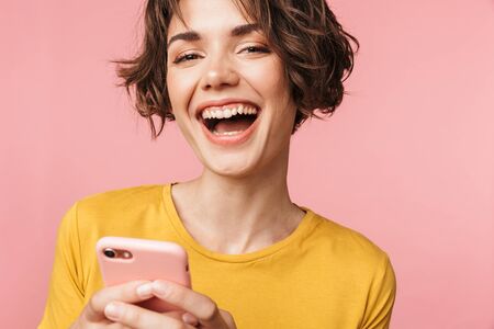 Image of a happy young beautiful woman posing isolated over pink wall background using mobile phone.の写真素材
