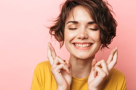 Image of young excited beautiful woman posing isolated over pink wall background make hopeful please gesture fingers crossed.の写真素材