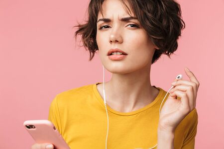 Image of a concentrated young beautiful woman posing isolated over pink wall background listening...