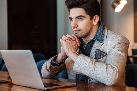 Image of a handsome young business man posing indoors in office using laptop computer.の写真素材