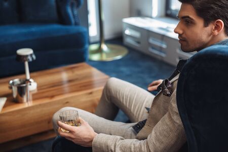 Back view image of a handsome young business man sitting in chair indoors in office drinking...