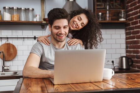 Picture of young couple man and woman 30s looking at laptop on table while having breakfast in kitchen at homeの写真素材
