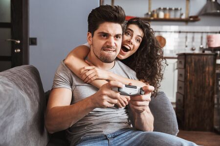 Image of european couple man and woman 30s sitting on sofa at home and playing video games together...