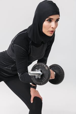 Image of young woman fitness muslim posing isolated over white wall background make exercises with dumbbell.の写真素材