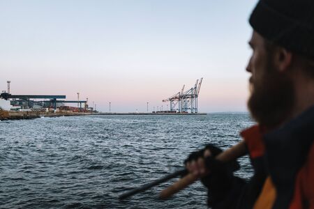Picture of a handsome man fisherman wearing coat and hat standing at the seashore. Focus on sea.