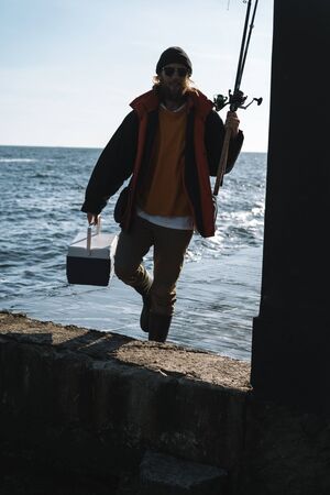 Silhouette of man fisherman wearing coat, holding rod, fishing at the beachの写真素材