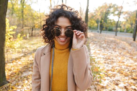 Smiling young african woman wearing autumn coat walking at the parkの写真素材