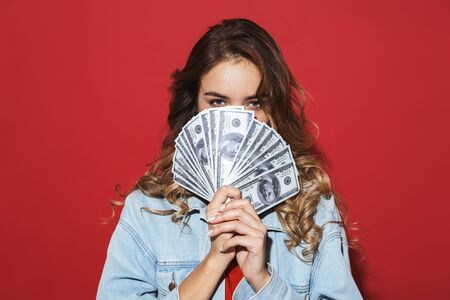 Portrait of a cheerful stylish young woman wearing denim jacket standing isolated over red...