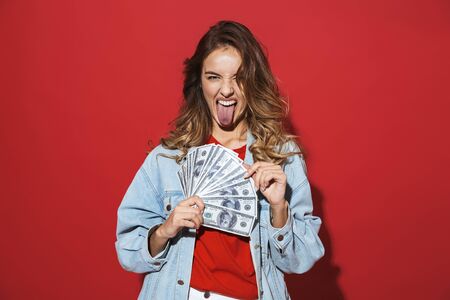 Portrait of a cheerful stylish young woman wearing denim jacket standing isolated over red...