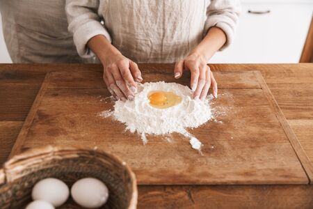 Portrait of attractive couple man and woman 30s wearing aprons cooking pastry with flour and eggs in...