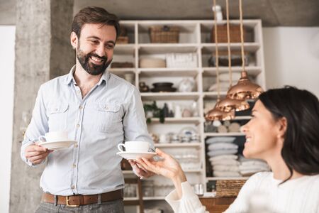 Portrait of beautiful happy couple man and woman 30s drinking coffee while having breakfast in kitchen at homeの写真素材