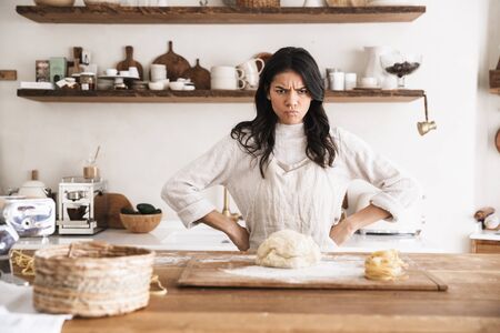 Portrait of angry european woman 30s wearing apron cooking and making homemade pasta of dough in kitchen at homeの写真素材