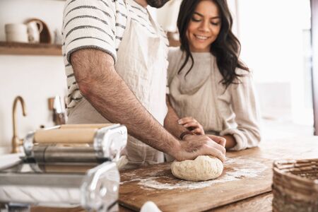 Portrait of caucasian couple man and woman 30s wearing aprons mixing the dough while cooking together in kitchen at homeの写真素材
