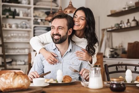 Portrait of modern european couple man and woman 30s eating at table while having breakfast in kitchen at homeの写真素材