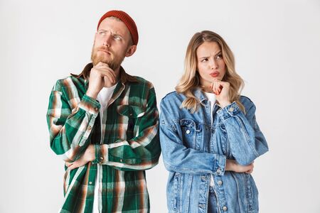 Photo of a thinking young loving couple posing isolated over white wall background.