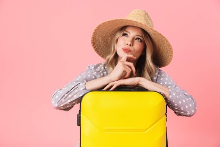 Image of a thinking young pretty woman tourist posing isolated over pink wall background with suitcase.の写真素材
