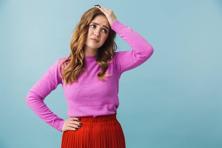 Beautiful confused young girl wearing casual clothes standing isolated over blue backgoundの写真素材