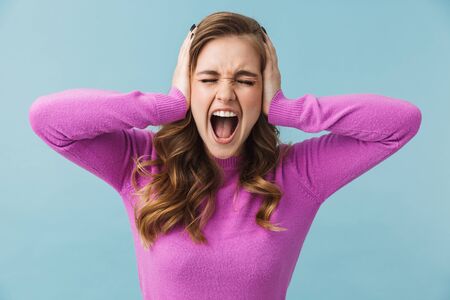 Beautiful annoyed young girl wearing casual clothes standing isolated over blue backgound, cover earsの写真素材