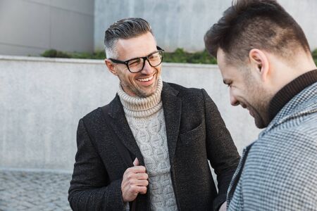 Two handsome men wearing coats spending time outdoors, talking