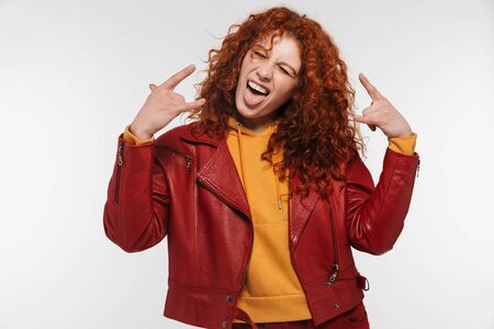 Portrait of crazy redhead woman 20s wearing leather jacket smiling and sticking out her tongue isolated over white backgroundの写真素材