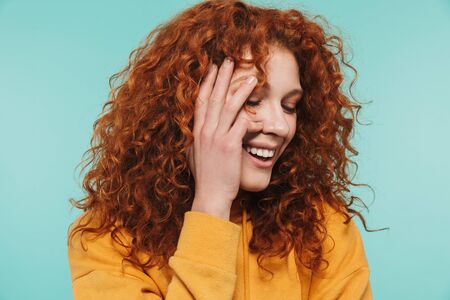 Photo closeup of modest woman 20s with curly ginger hair smiling at camera isolated over blue backgroundの写真素材
