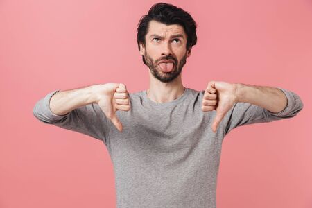 Portrait of an upset bearded man standing isolated over pink background, showing thumbs downの写真素材