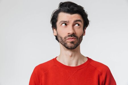 Handsome pensive young bearded brunette man wearing sweater standing isolated over white background, thinkingの写真素材