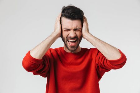 Handsome young bearded brunette man wearing sweater standing isolated over white background, having headacheの写真素材