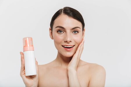 Beauty portrait of an attractive young brunette woman standing isolated over white background, showing bottle with facial oilの写真素材