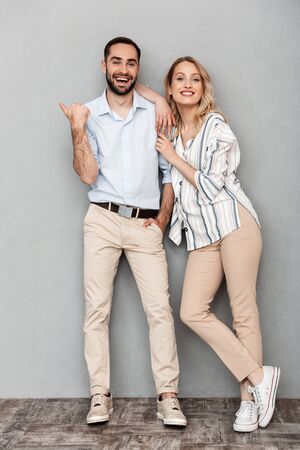 Full length image of charming european couple in casual clothing smiling and looking at camera isolated over gray backgroundの写真素材