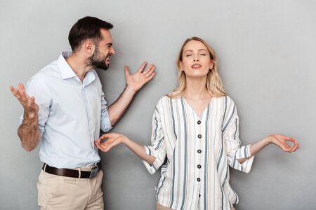 Photo of angry man in casual clothes screaming at calm woman isolated over gray backgroundの写真素材