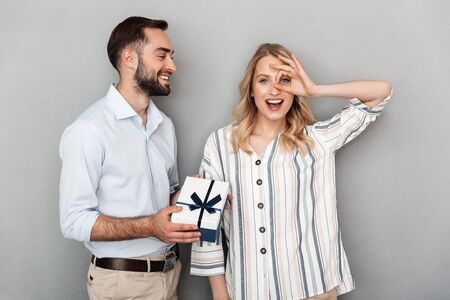 Photo closeup of unshaven man in casual clothing smiling and giving present to woman isolated over gray wallの写真素材