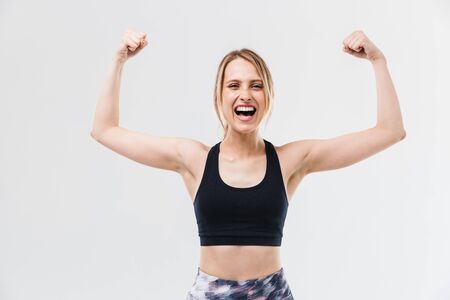 Image of excited blond woman 20s dressed in sportswear working out and doing exercises with dumbbells during fitness in gym isolated over white wallの写真素材