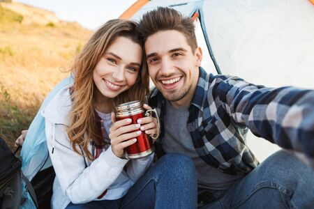 Photo of happy young loving couple outside in free alternative vacation camping drinking hot tea.の写真素材
