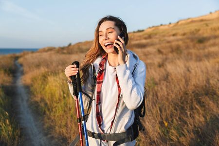 Happy young girl carrying backpack, hiking, talking mobile phoneの写真素材