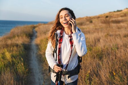 Happy young girl carrying backpack, hiking, talking mobile phoneの写真素材