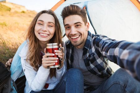 Photo of happy young loving couple outside in free alternative vacation camping drinking hot tea.の写真素材