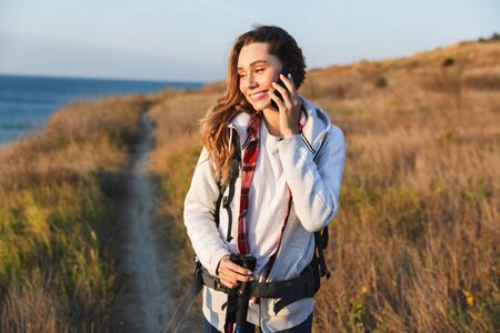 Happy young girl carrying backpack, hiking, talking mobile phoneの写真素材