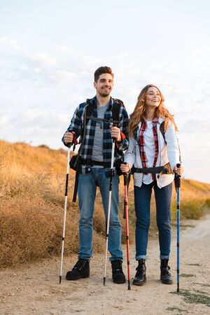 Cheerful young couple carrying backpacks hiking together, walking on a trailの写真素材