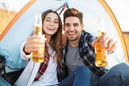 Photo of happy young loving couple outside in free alternative vacation camping drinking beer.の写真素材