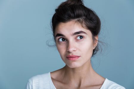 Close up portrait of a pensive unsatisfied pretty young brunette woman wearing white t-shirt standing isolated over blue backgroundの写真素材