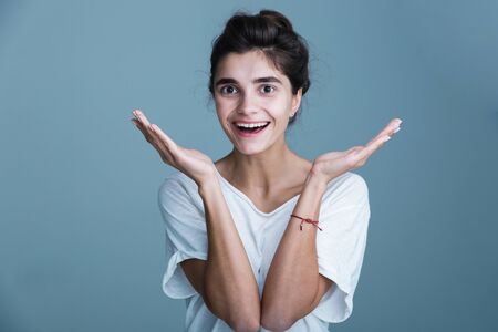 Close up portrait of a pretty smiling young brunette woman wearing white t-shirt standing isolated over blue background, looking at cameraの写真素材