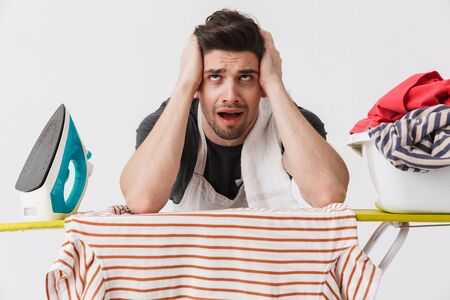 Image of a tired bored young houseman househusband with iron and clothes isolated over white wall background.の写真素材