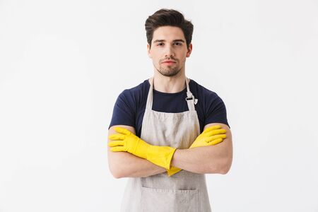 Photo of joyful young man wearing yellow rubber gloves for hands protection smiling at camera while cleaning house isolated over white backgroundの写真素材