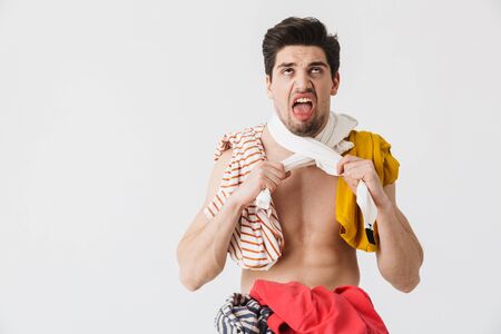 Handsome angry brunette houseman wearing apron standing isolated over white background, choking himself with clothesの写真素材