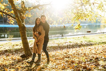 Cheerful young couple spending fun time at the park in autumn, playing with leavesの写真素材