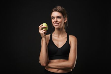 Attractive smiling young healthy fitness woman wearing sports bra and shorts isolated over blackの写真素材