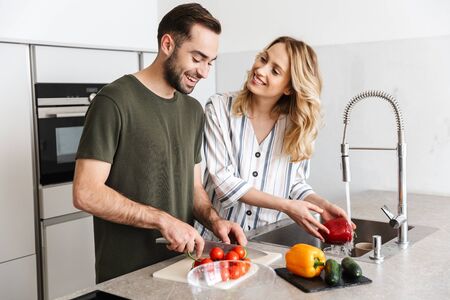 Photo of a cheerful pleased young loving couple indoors at the kitchen cooking vegetable salad have a breakfast.の写真素材