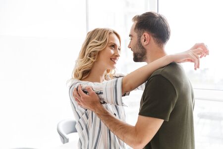 Image of a happy young loving couple posing at the kitchen at home hugging.
