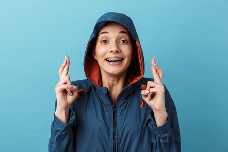 Cheerful young woman wearing a jacket standing isolated over blue background, holding fingers...
